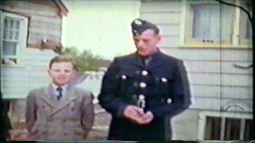 Vintage home movie of two uniformed men posing with a young boy outside a suburban house as the camera pans to a child on the front steps