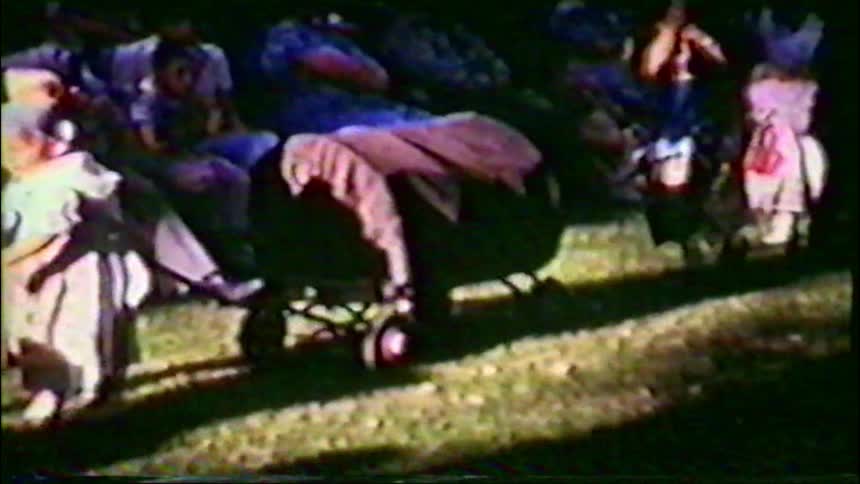 A charming vintage home movie captures children in a variety of colorful costumes participating in an outdoor parade