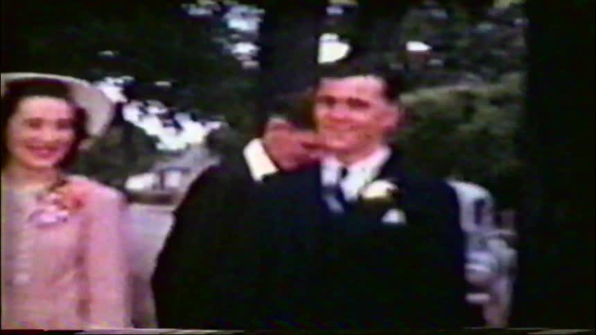 Vintage home movie footage from the 1940s captures a smiling bride and groom in a military uniform posing with their wedding party