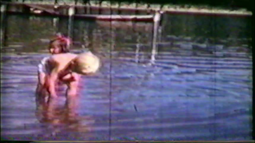 Archival home movie footage captures the innocent joy of two young toddlers playing in a lake on a summer day