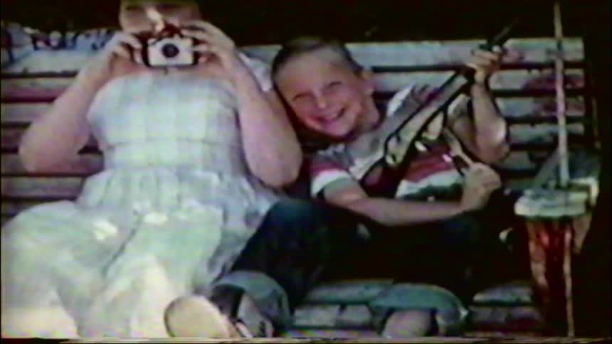 Three children pose for a picture on a porch swing with a vintage camera and a toy rifle in this charming home movie from the 1950s