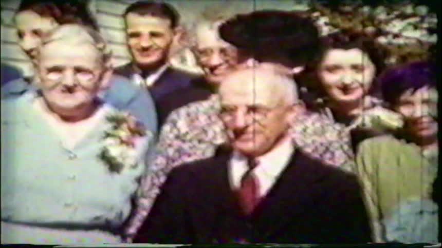 A multi-generational family smiles and poses together for a photo on a sunny day in the 1940s