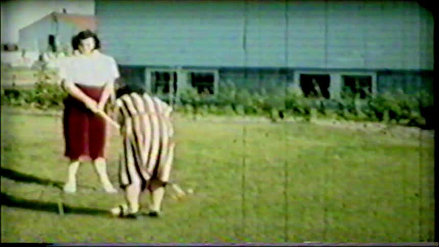 Vintage 1950s home movie footage captures two women enjoying a leisurely game of croquet in their backyard on a sunny day