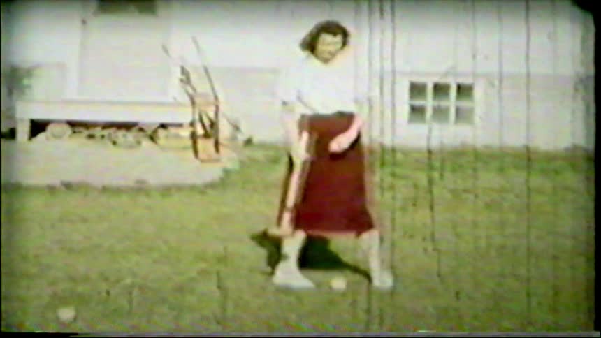 Vintage footage captures a woman in a skirt playing a casual game of croquet in a sunny backyard