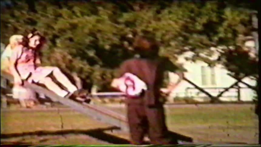 Vintage home movie captures children playing on a slide and seesaw at a park on a sunny day