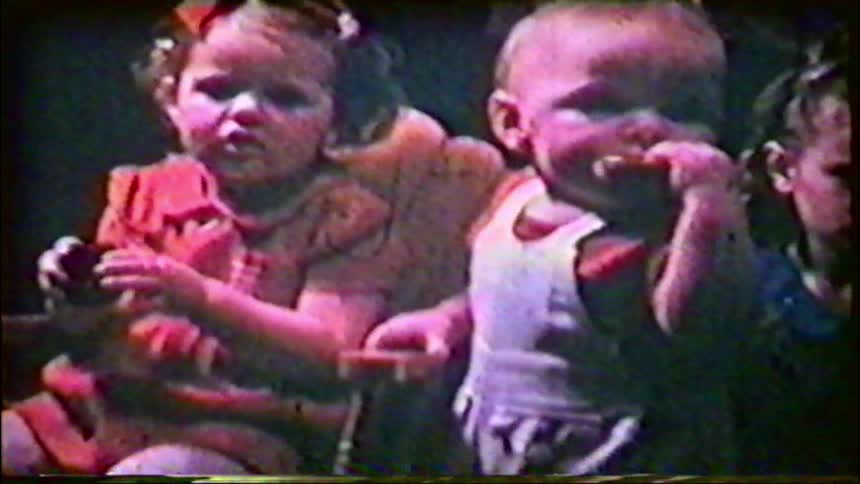 Authentic vintage home movie footage shows a group of toddlers sitting together and eating a snack