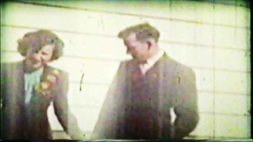 An old, damaged 8mm film shows a happy couple in formal attire smiling and sharing a moment together