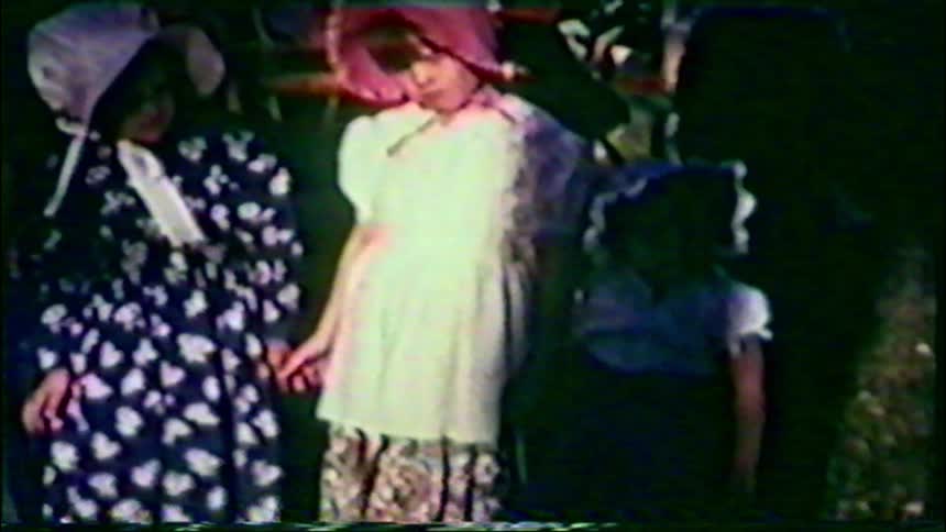 A grainy home movie captures young children dressed in colonial-era costumes for a historical reenactment or school play