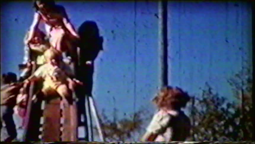 Nostalgic vintage footage shows young children playing on a slide in a park on a sunny day
