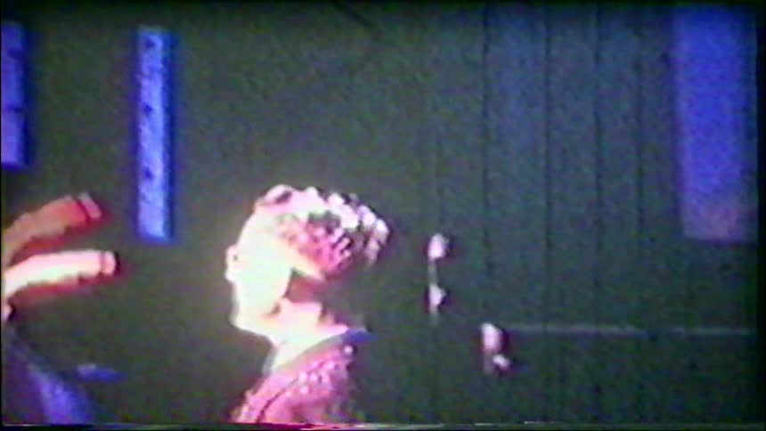 A heavily distorted and grainy vintage film shows a bride and groom feeding each other wedding cake