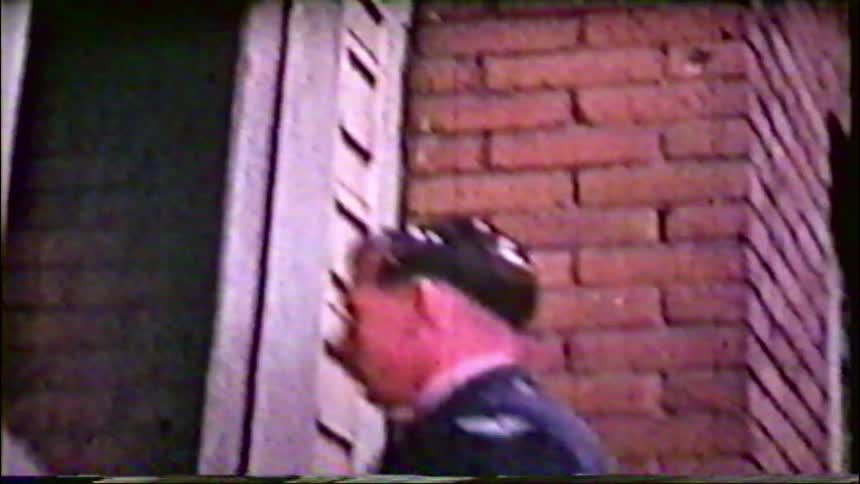 A vintage home movie captures a bride in her wedding dress and the groom leaving a brick building with guests on their wedding day