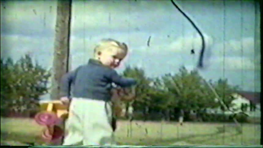 Vintage home movie footage from the 1950s shows a little blonde boy playing with a yellow toy truck in the sand