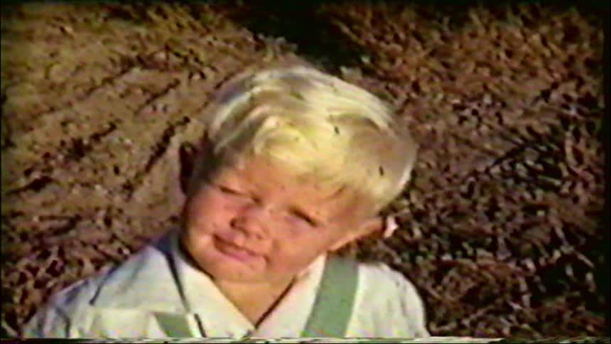 Vintage home movie footage shows a close-up of a young blonde boy with a dirty face making funny expressions