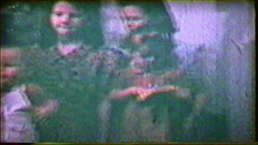 A vintage home movie from the 1950s captures a family with young children posing together inside their home