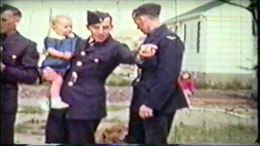 Vintage footage shows soldiers in uniform holding their young children and petting a dog outside