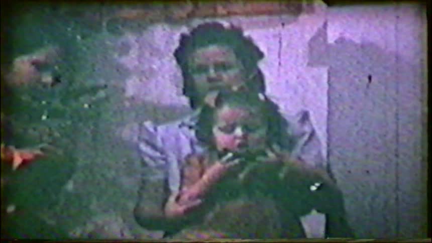 A mother lovingly holds her little girl next to a Christmas tree in this grainy, vintage home movie from the 1940s