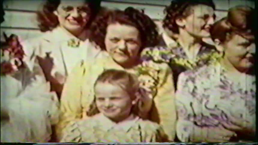 A vintage 1940s home movie captures a smiling bride and groom posing for a group photo with their wedding guests outside