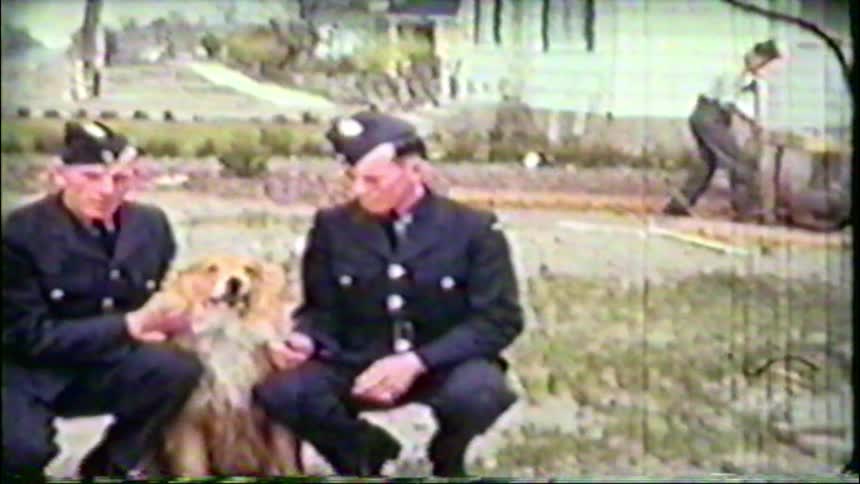 Vintage footage of three soldiers in uniform petting a friendly, fluffy dog outdoors at their barracks