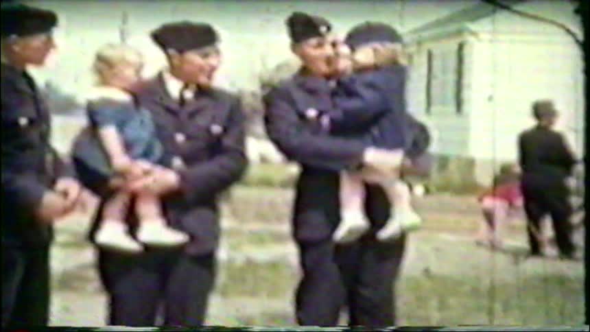 Nostalgic home movie footage shows three soldiers in uniform smiling and holding two small children