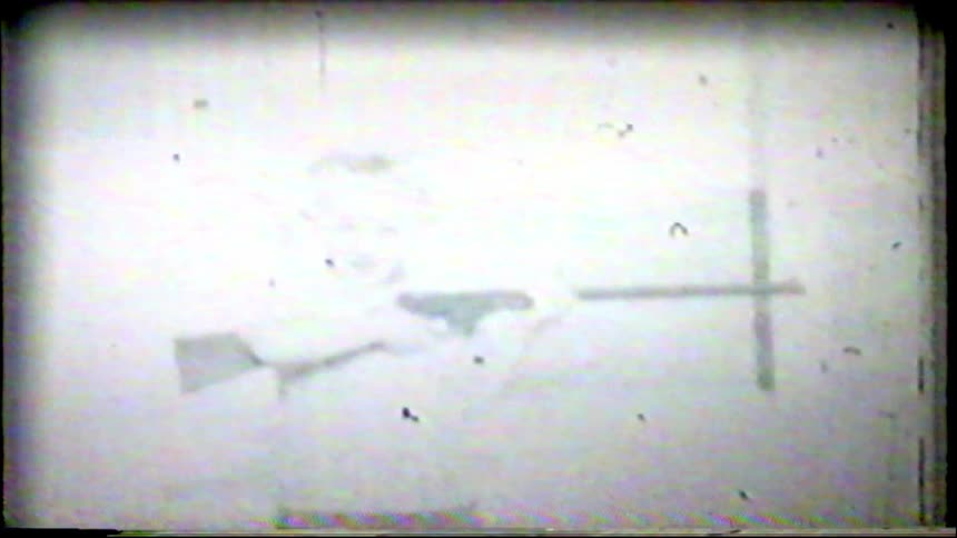 An overexposed, grainy black and white archival clip shows a young boy proudly aiming his toy rifle