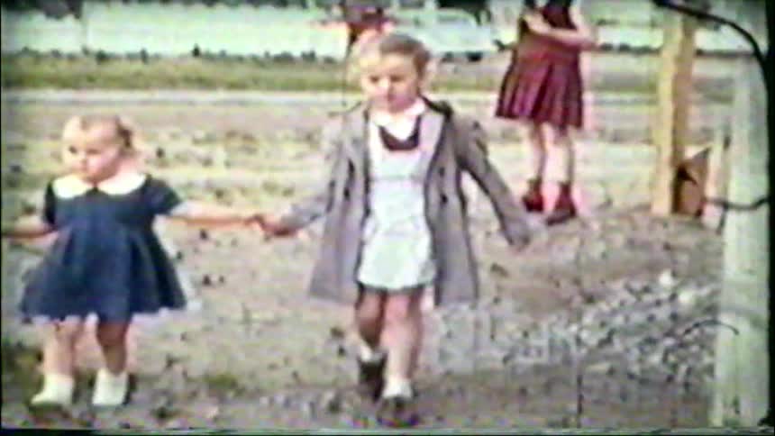 Charming vintage footage shows two young sisters holding hands as they walk toward the camera in a rustic yard