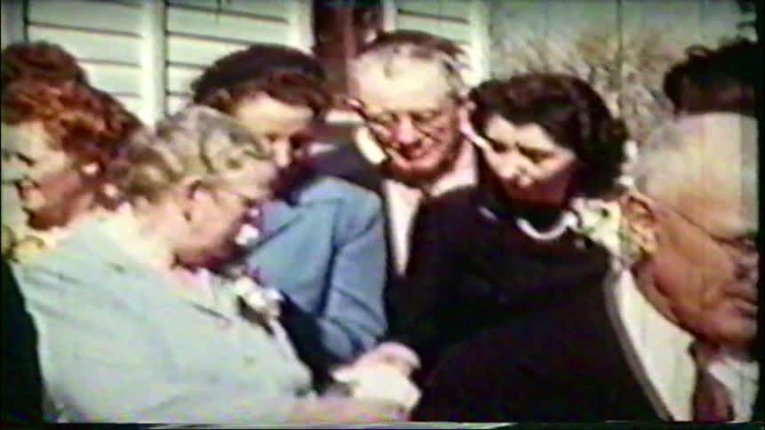 A vintage home movie from the 1940s captures a large, multi-generational family gathering together outdoors
