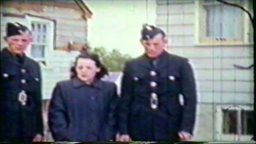 Vintage home movie footage shows two soldiers in uniform posing with a woman outside a house