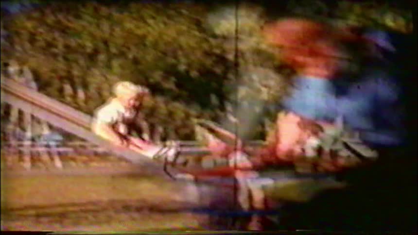 A toddler slides down a tall metal slide at a sunny park in this nostalgic vintage home movie footage