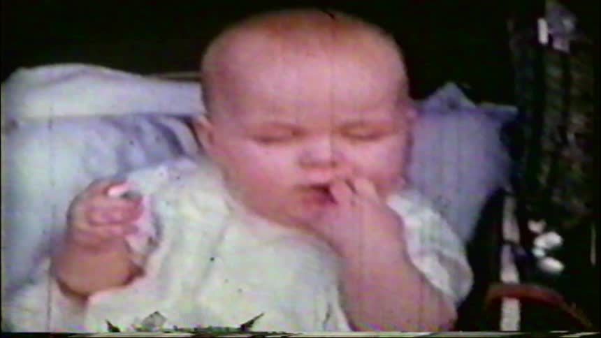 A close-up of an expressive baby with chubby cheeks sitting in a pram, from a vintage 1950s home movie