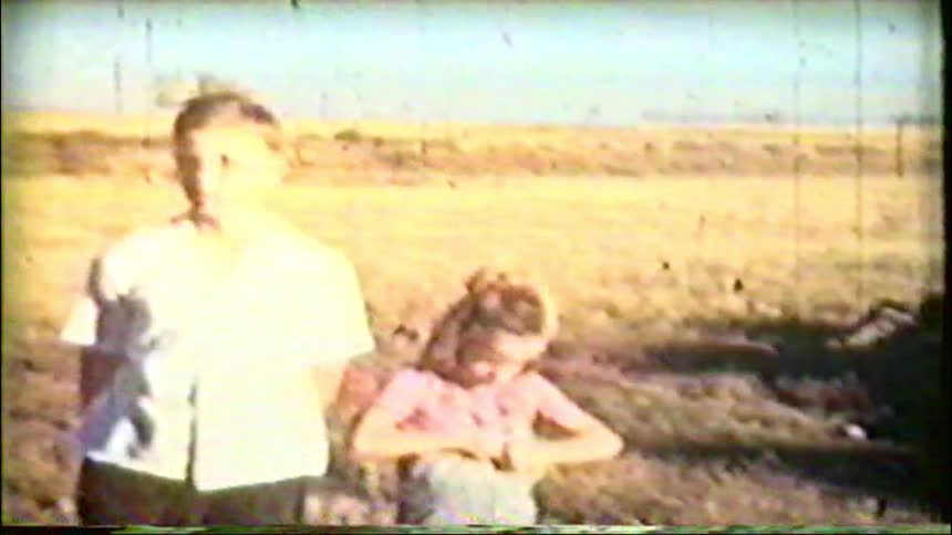 A young boy and girl stand together in a sunny, dry field in this charming vintage home movie