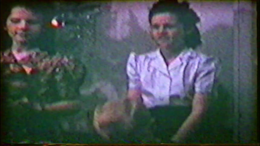 Vintage footage shows a mother and her children laughing and smiling together in front of their Christmas tree