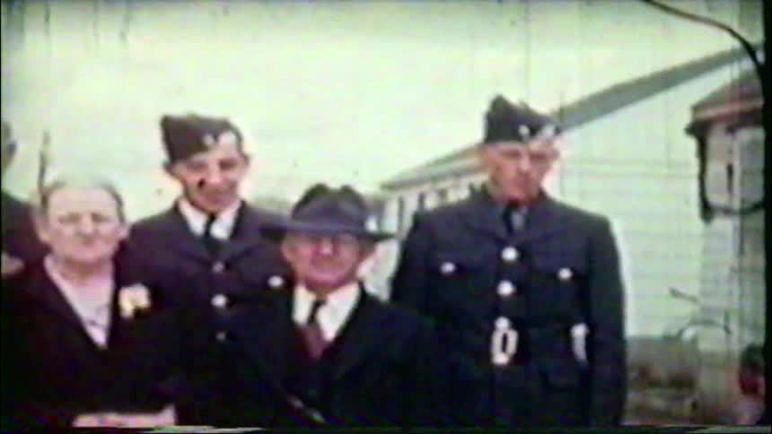 A vintage home movie captures a family portrait with two soldiers in uniform from the World War II era