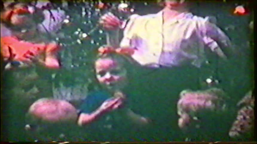 A grainy vintage home movie captures a family with young children celebrating Christmas together around their decorated tree