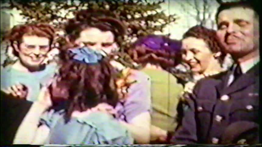 A vintage home movie from the 1940s shows a large group of family and friends smiling and socializing outdoors