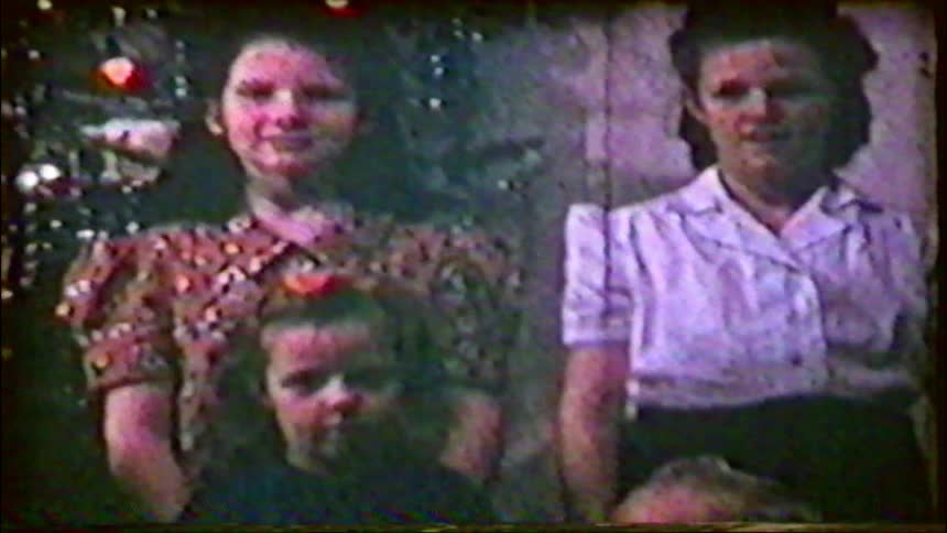 A vintage home movie from the 1940s shows a family posing for a Christmas portrait in front of their decorated tree