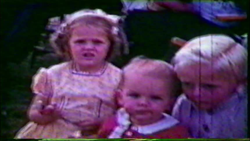 A sweet vintage home movie shows a group of children and a baby gathered together on the lawn during a sunny day