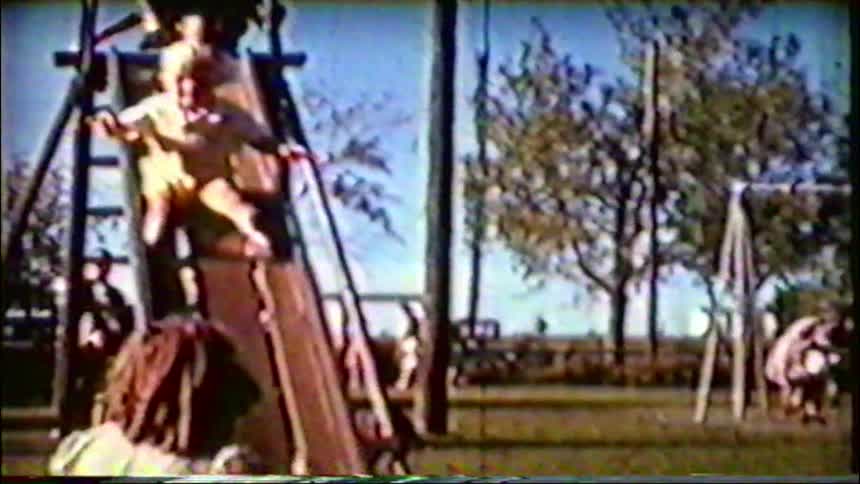 Nostalgic home movie footage shows young children taking turns going down a tall playground slide