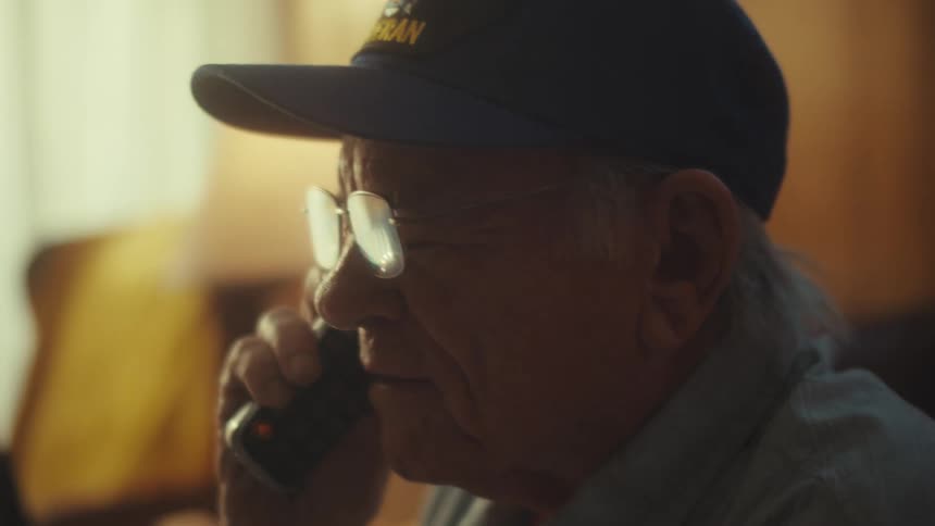 Close up of an elderly veteran wearing a cap and glasses having a serious conversation on a cordless phone