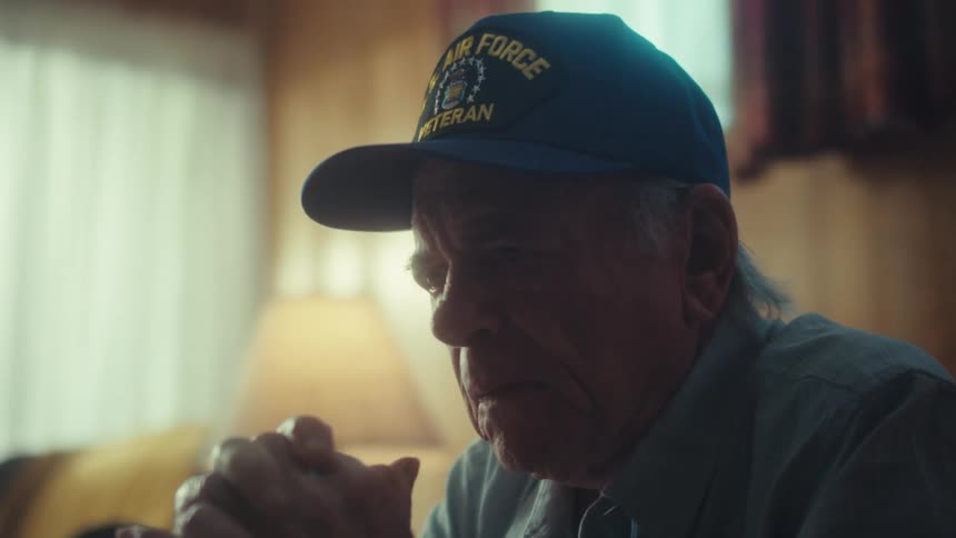 A sad and thoughtful elderly Air Force veteran sits alone in his dimly lit living room, reflecting on his past
