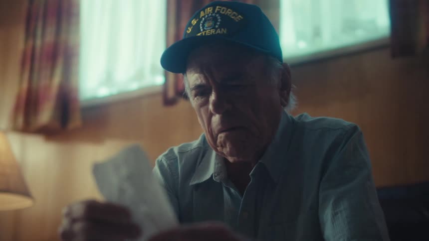 A concerned elderly Air Force veteran reads a letter in his home and becomes visibly upset, crumpling the paper in distress
