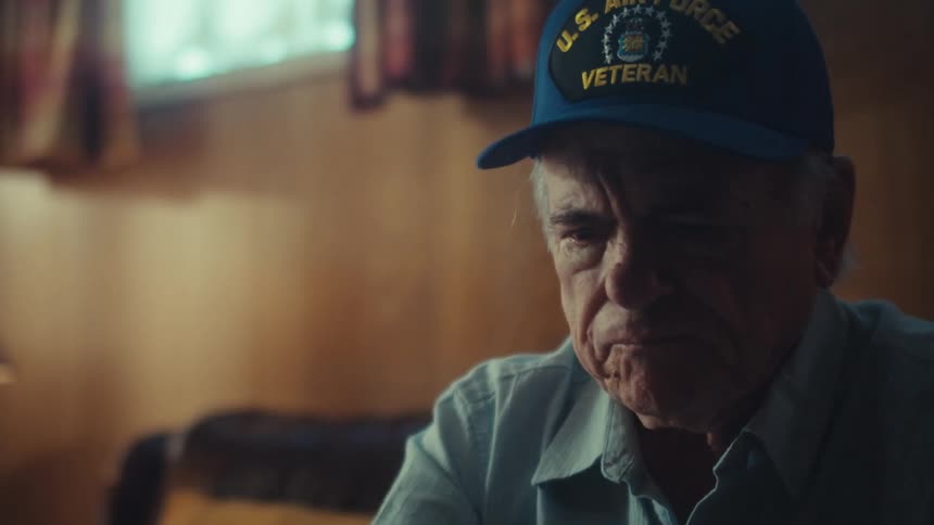 A close-up shot of a worried elderly U.S. Air Force veteran rubbing his face in distress while reviewing his finances