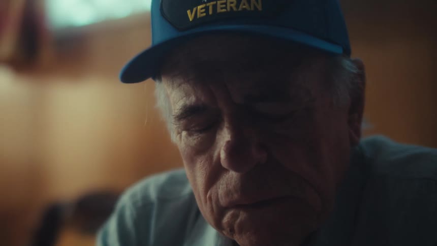 A pensive elderly veteran sits alone in his dimly lit living room, his face showing the weight of worry and emotion