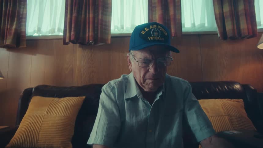 Slow zoom on the concerned face of an elderly U.S. Air Force veteran as he sorts through a pile of bills and receipts on his coffee table