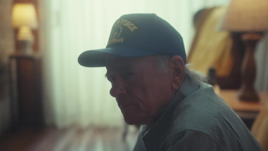 A pensive elderly Air Force veteran sits alone in his dimly lit home, reflecting on his memories