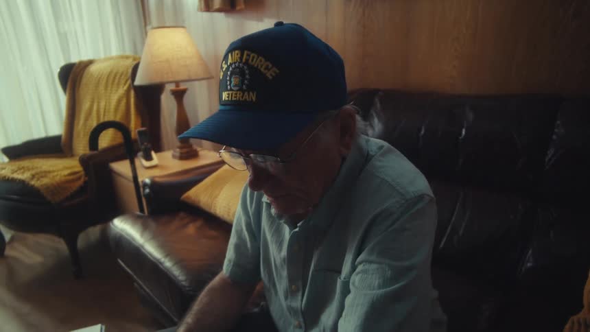 A concerned elderly Air Force veteran puts on his glasses to review his finances in his dimly lit living room