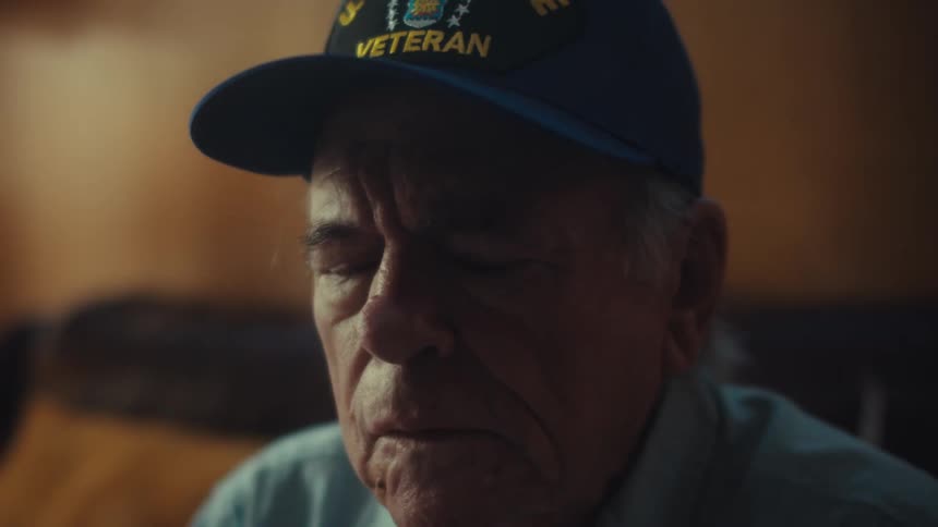 A somber elderly U.S. Air Force veteran sits in a dimly lit room, his face etched with deep thought as he reflects on his memories