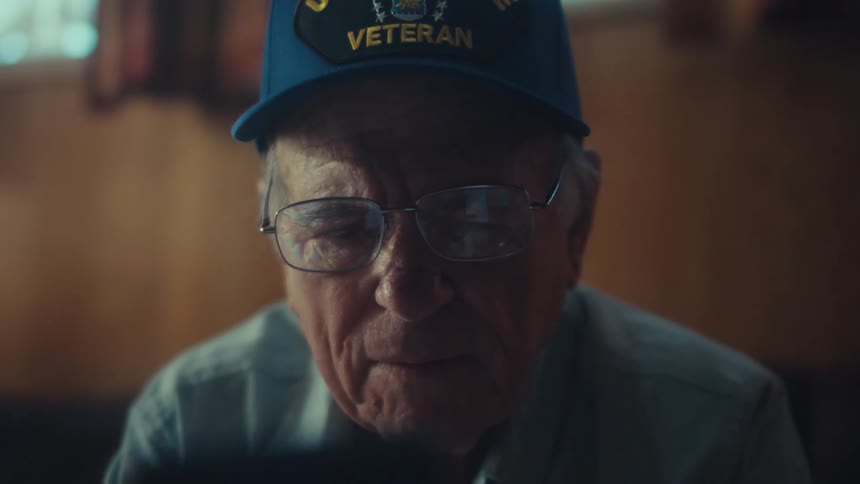 A close-up of a thoughtful elderly U.S. Air Force veteran scrolling on his smartphone in a dimly lit room