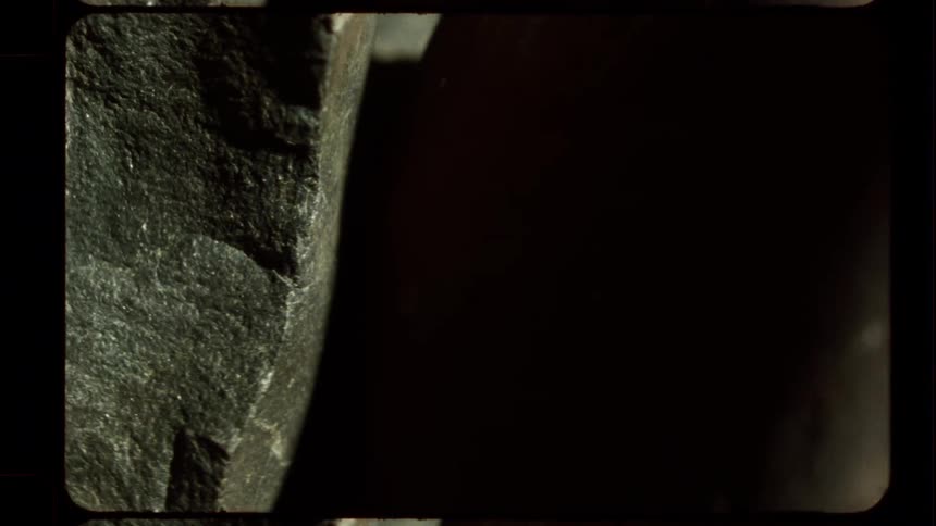 Light slowly fades over a mysterious, abstract rock formation in a grainy, vintage film close-up