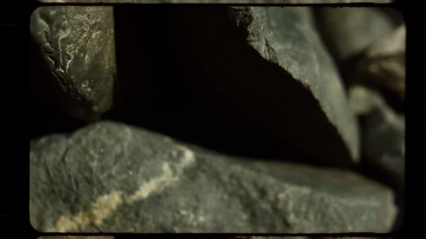 An atmospheric macro shot of gray rocks with dramatic shadows, captured with a vintage film aesthetic