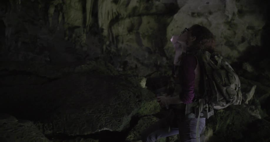 Woman wearing backpack exploring cave with flashlight blinking red light